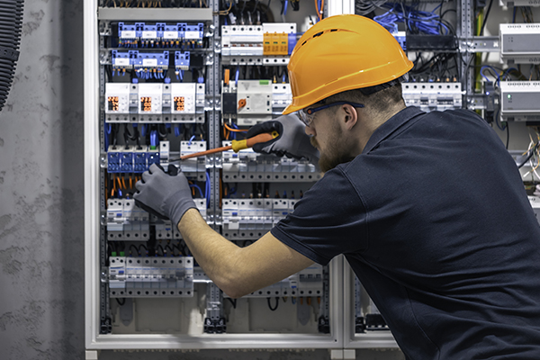 Young adult electrician civil engineer screwing equipment into fuse box.